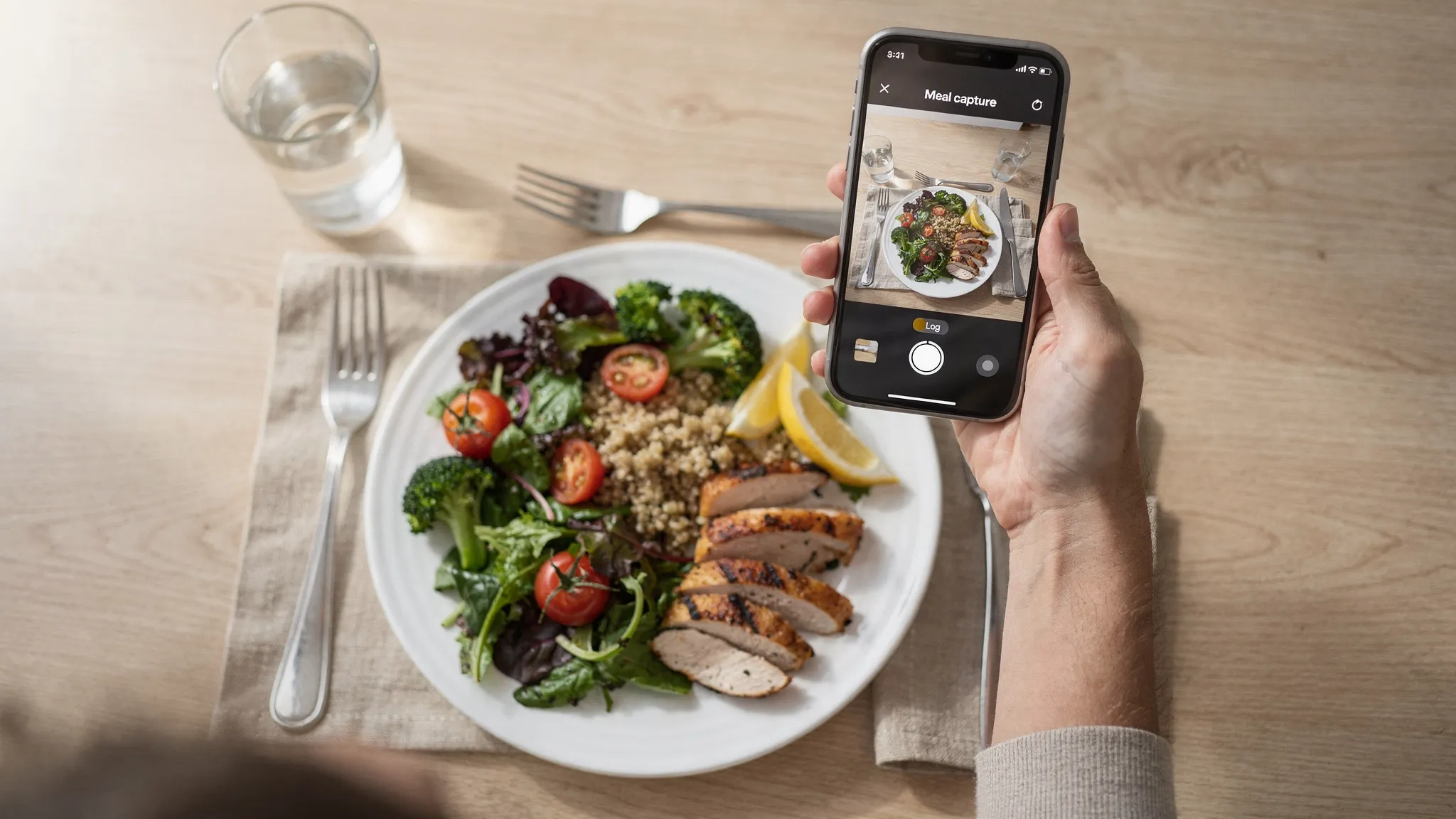 A person holding a smartphone capturing a photo of a colorful meal for nutrition logging.